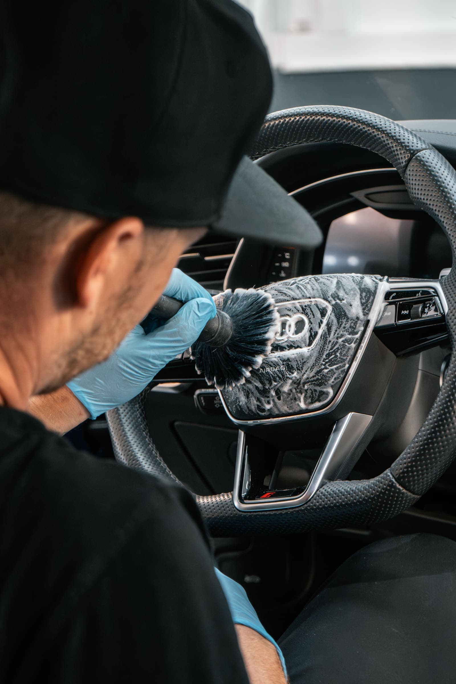 Detailer v rokavicah z mehko krtačo čisti volan avtomobila